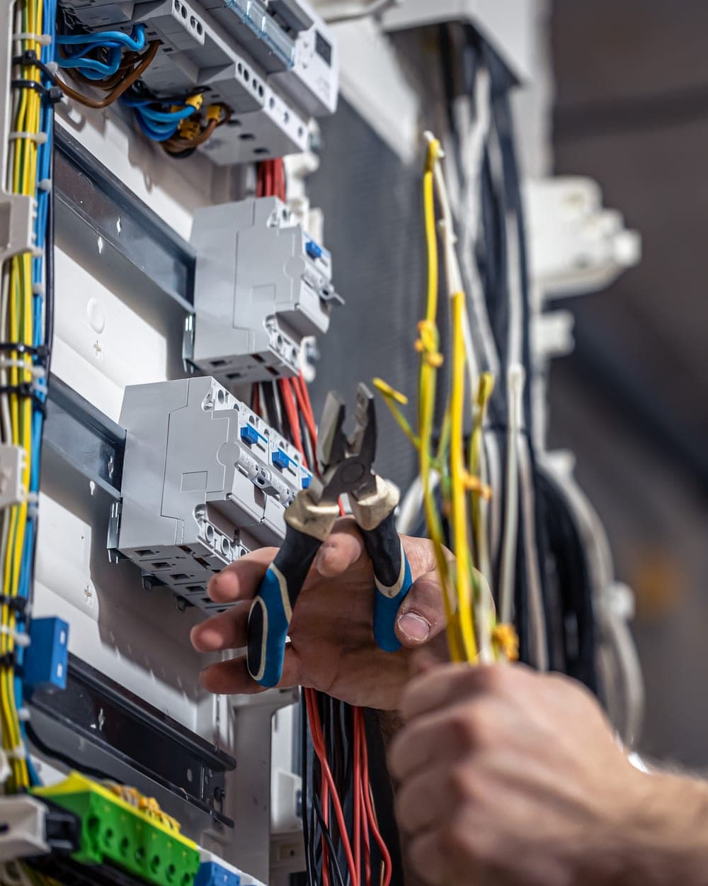 An electrician's hands cutting cable inside an open consumer unit
