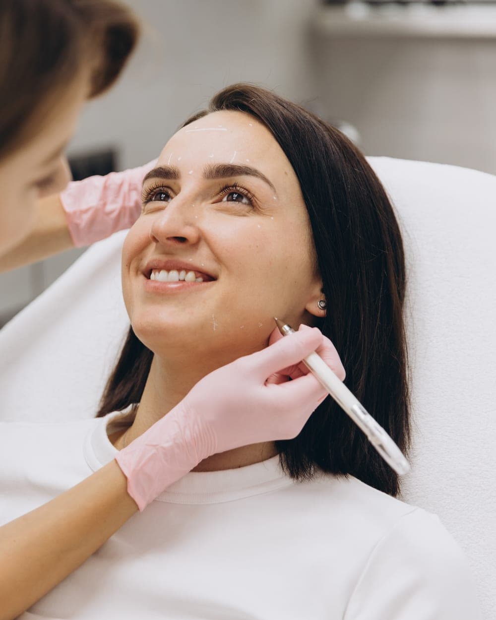 A practitioner marking up a client's face during a treatment in a clinic room